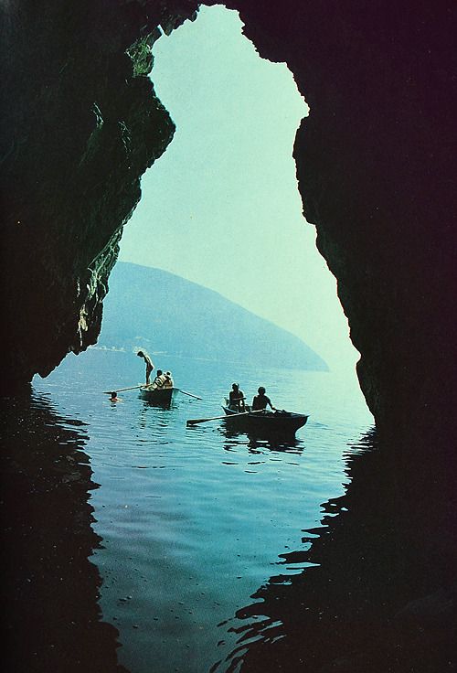 Boats on blue water seen from inside a cave